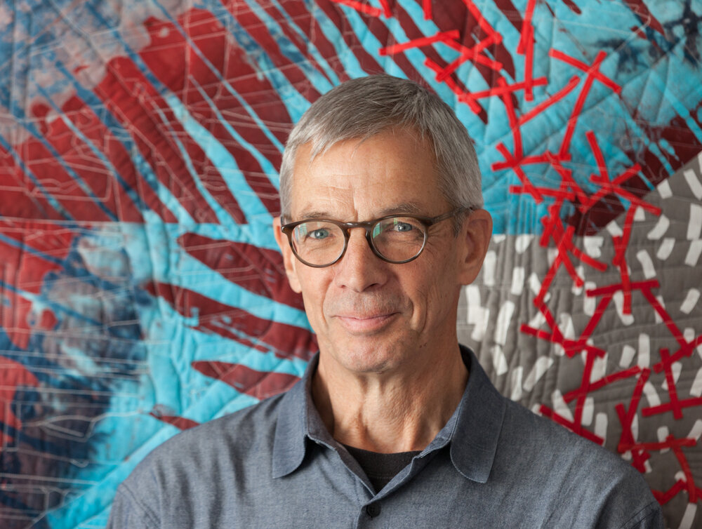 Joe Cunningham in front of red, blue, grey, and white quilt.